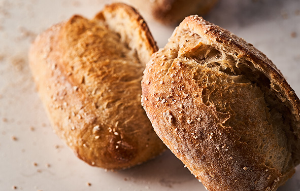 Deux pains individuels à la croûte dorée et farinée, posés sur une surface claire.