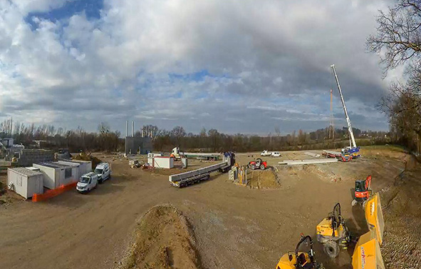 Outdoor construction site with construction machinery, a crane, and materials, under a cloudy sky.