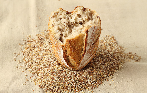Cereal bread cut in half, showing an open crumb, placed on a bed of grains, with a golden, floured crust.