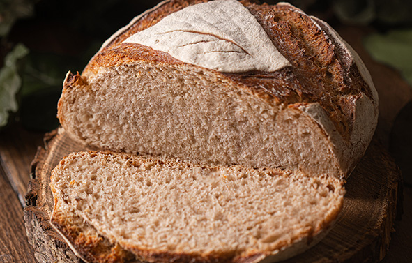 Partially sliced round bread, showing a dense, light-colored crumb, placed on a wooden board.