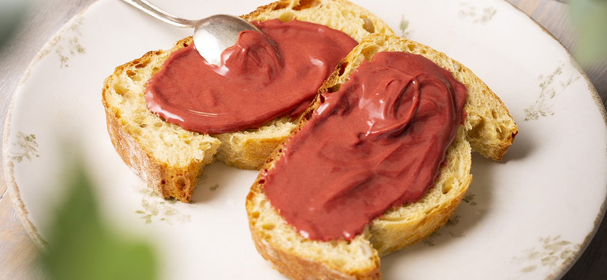 Two slices of brioche spread with raspberry spread, presented on a white plate with a spoon above.