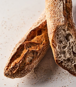 Deux baguettes de pain, dont une coupée, montrant une mie alvéolée et une croûte dorée, posées sur une surface claire.