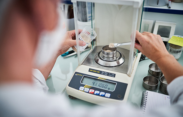 Pesée précise d’un échantillon de poudre sur une balance de laboratoire, réalisée par un opérateur dans un environnement de recherche et d’analyse.