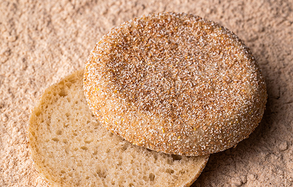 English muffin coated with Phil hulled-wheat semolina, with one half cut to reveal the crumb, placed on Phil hulled-wheat semolina.