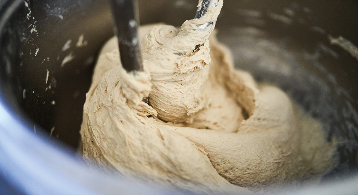 Dough being kneaded inside a stainless-steel industrial mixer.
