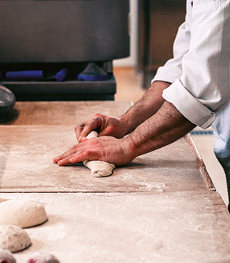Hands shaping a dough ball on a floured work surface, with other pieces of dough visible nearby.