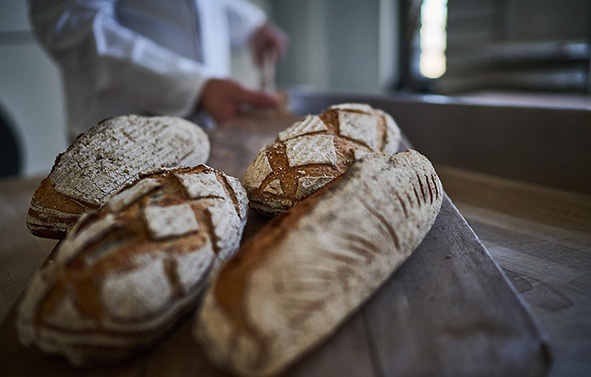 Four breads coming out of the oven on a wooden peel