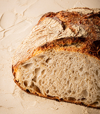 Pain rond coupé, montrant une mie alvéolée et une croûte dorée et farinée, posé sur une surface claire.