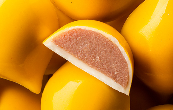 Caramelos amarillos cortados por la mitad, mostrando un corazón de gelatina rosa, vistos en primer plano.