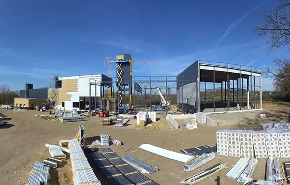 Chantier de construction en extérieur avec engins de chantier, grue et matériaux, sous un ciel nuageux.