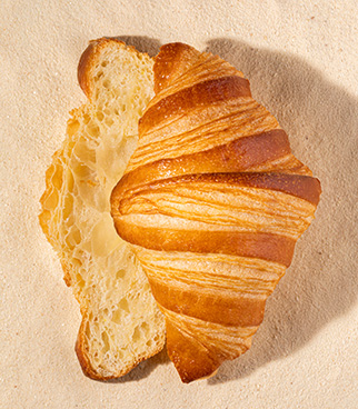 Golden croissant seen from above, partially opened, showing an airy crumb, placed on a light surface.