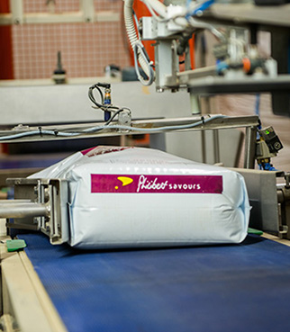 Bolsa de producto envasado sobre una cinta transportadora automática, en una línea de envasado industrial, con máquinas visibles alrededor.