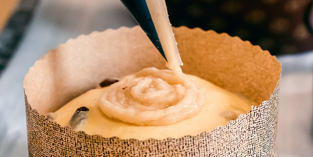 Preparation of macaronade piped onto the top of a raw panettone using a piping bag.