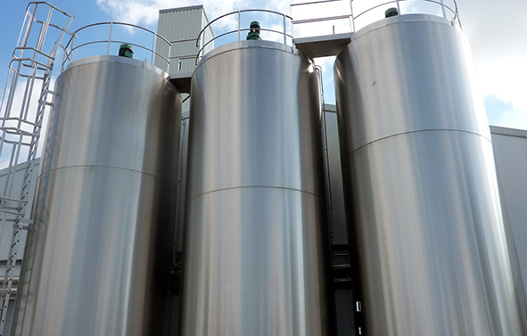 Three large stainless-steel industrial tanks installed outdoors, with visible walkways and ladders.