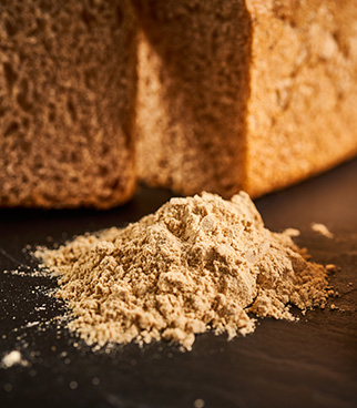 Tas de levain déshydraté posé sur une surface sombre, avec des tranches de pain floues en arrière-plan.