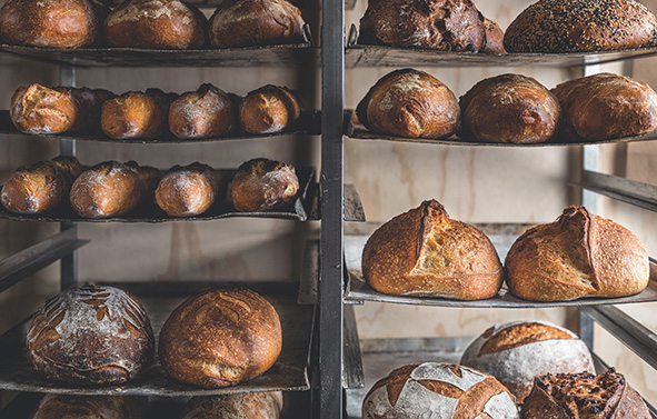 Breads of different shapes and sizes arranged on metal racks, placed on shelves in a bakery.