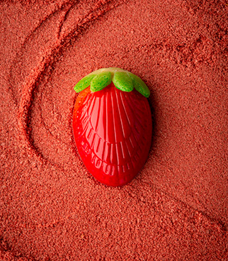 Strawberry-shaped red candy with a green leaf, placed on a surface of red powder.