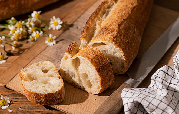Una baguette dorada sobre una tabla de madera en un ambiente primaveral