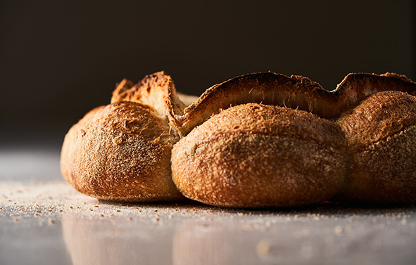 Pain rustique à la croûte dorée, vu de profil, posé sur une surface en marbre avec de la semoule de blé vêtue éparpillée.