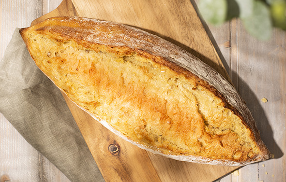 Pain au maïs allongé, à la croûte dorée et légèrement farinée, posé sur une planche en bois, vu de dessus.