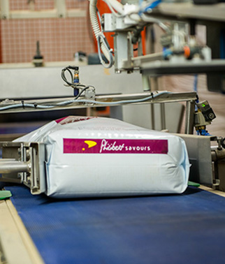 Packaged product bag on an automatic conveyor belt in an industrial packaging line, with machines visible around it.