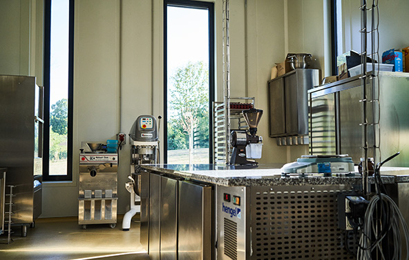 Atelier de production alimentaire avec des équipements industriels en inox, comprenant une table de travail, des machines de transformation et des contenants, dans un environnement propre et organisé.