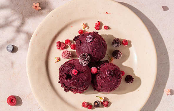 Blueberry sorbet ice cream with red berries, placed on a small plate.